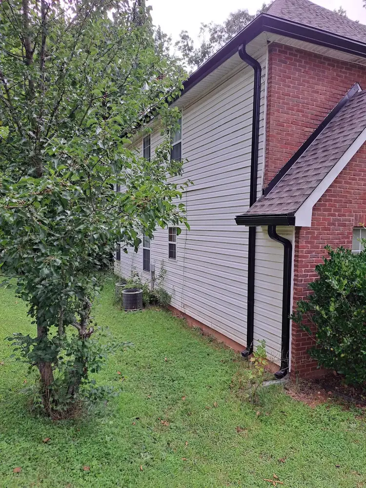 Dark gutters and downspouts installed on a brick and siding home